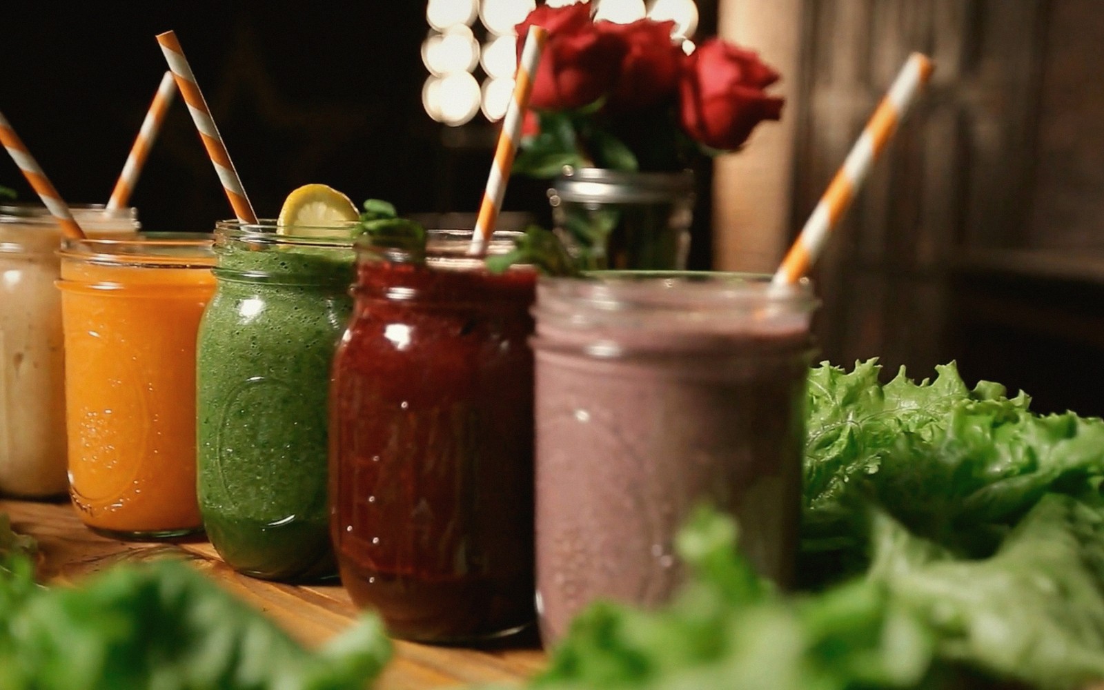 Five mason jars of colorful smoothies with striped straws lined up on a table